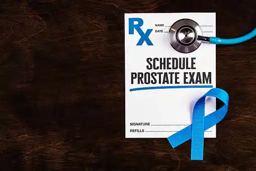 a medical form reading 'schedule prostate exam' with a stethoscope and a blue ribbon kept over it